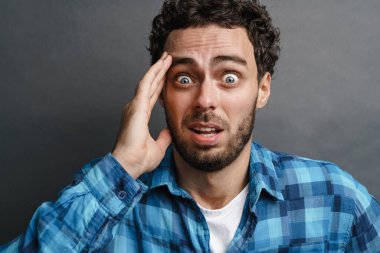 Şok olmuş yakışıklı adam gri arka planda mahsur kalmış kamerada şaşkınlığını ifade ediyor.