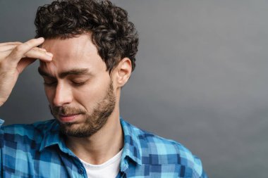 Tıraşsız yakışıklı, başı ağrıyan, kameraya poz veren, gri arka planda izole edilmiş.