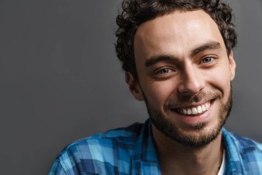 Neşeli yakışıklı adam gülümsüyor ve gri arka planda izole edilmiş kameraya bakıyor.