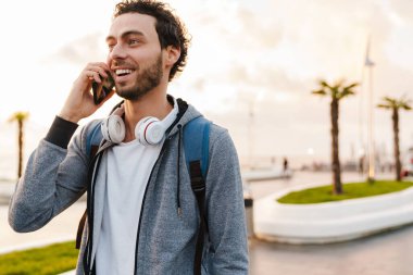 Gezinti güvertesinde yürürken gülümseyen ve telefonla konuşan neşeli genç adam.