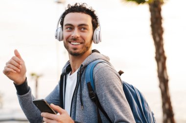 Gülümseyen adam başparmağını kaldırıyor ve gezinirken cep telefonu kullanıyor.