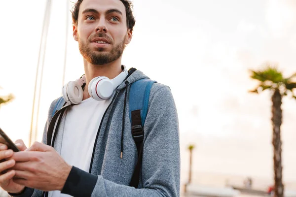 Ευχαριστημένος Νεαρός Ακουστικά Που Χρησιμοποιεί Κινητό Του Ενώ Περπατάει Περιπάτους — Φωτογραφία Αρχείου