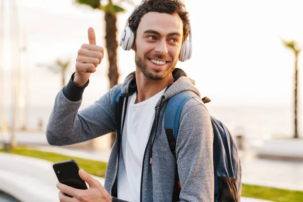 Gülümseyen adam başparmağını kaldırıyor ve gezinirken cep telefonu kullanıyor.