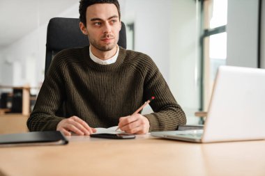 Bir ofiste dizüstü bilgisayar ve belgelerle çalışan girişimci,