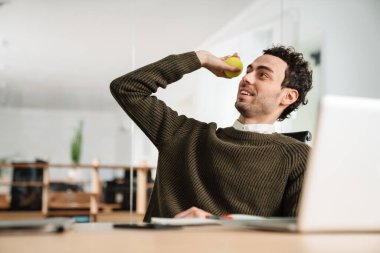 Gülümseyen genç adam, ofis masasına tenis topu atıyor.