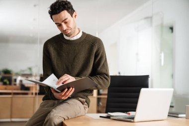 Bir ofiste dizüstü bilgisayar ve belgelerle çalışan girişimci