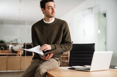 Ofiste çalışan kendinden emin genç bir yönetici, elinde belgeler var.