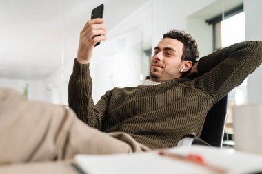 Ofisteki masada otururken cep telefonuyla görüntülü konuşma yapan kendine güvenen genç bir yönetici.