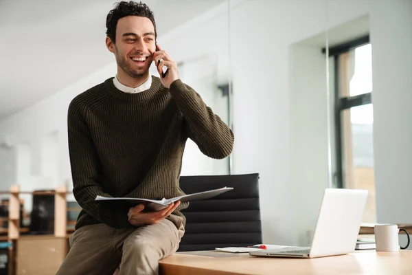 Sorrindo Confiante Jovem Empreendedor Sentado Mesa Escritório Falando Celular Segurando — Fotografia de Stock