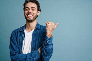 Mavi arka planda tek başına dikilirken fotokopi alanını gösteren kendinden emin bir gencin portresi.