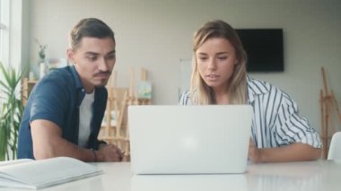 Çekici erkek ve kadın, sanat stüdyosundaki masada otururken dizüstü bilgisayardan bir şey izliyorlar.