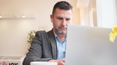 Yakışıklı bir yetişkin adam laptopuyla bir kafede masada oturuyor.