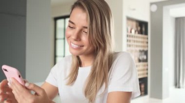 Mutlu bir kadın akıllı telefonunu evde masada otururken kullanıyor.