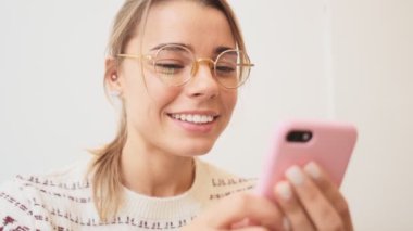 Gülümseyen bir kadın içerideki kafede oturmuş akıllı telefonuyla yazı yazıyor.