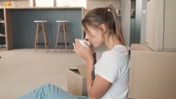 Μια Ευχαριστημένη Γυναίκα Πίνει Καφέ Ενώ Κάθεται Στο Πάτωμα Κοντά — Αρχείο Βίντεο