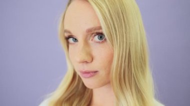 Gülümseyen sarışın bir kadının yakın çekim görüntüsü stüdyodaki beyaz arka planda tek başına duran kameraya bakıyor.