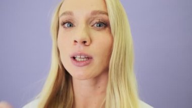 Güzel sarışın bir kadının yakın çekim görüntüsü stüdyoda beyaz arka planda tek başına duran kameraya hava öpücüğü gönderiyor.