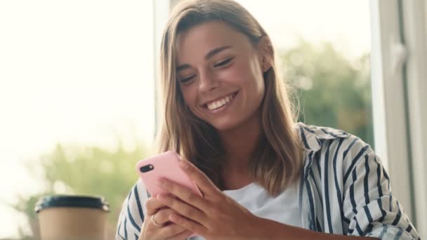 Uma Jovem Feliz Está Usando Seu Smartphone Enquanto Bebe Café — Vídeo de Stock