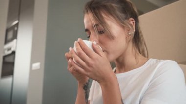 Güzel bir kadının yakın çekim görüntüsü evde yerde otururken kahve içmesidir.