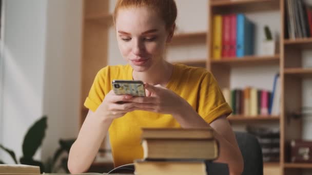幸せな若い赤毛の女性はオフィスに座っている彼女のスマートフォンを使用しています — ストック動画
