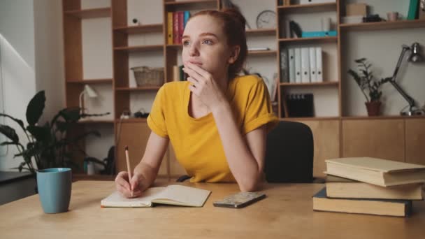 若い赤毛の女性がオフィスのテーブルに何か書いてる — ストック動画
