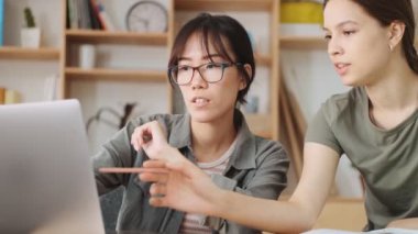 Ciddi kadın iş arkadaşları ofiste çalışırken dizüstü bilgisayar kullanarak bir şeyler tartışıyorlar.