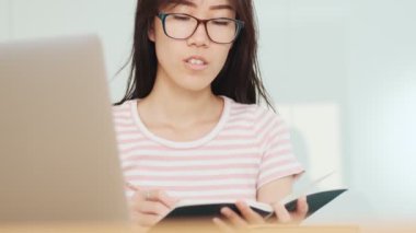 Odaklanmış Asyalı bir kadının kırpılmış görüntüsü ofisteki masada oturan deftere bir şey yazıyor.