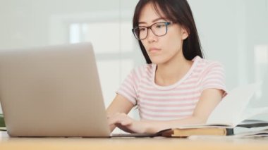 Ofiste dizüstü bilgisayarla çalışırken kafası karışık Asyalı bir kadın masada oturuyor.