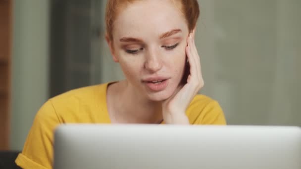 中に座っている間に彼女のラップトップコンピュータを見ている間 幸せな若い赤毛の女性は夕食を取っています — ストック動画