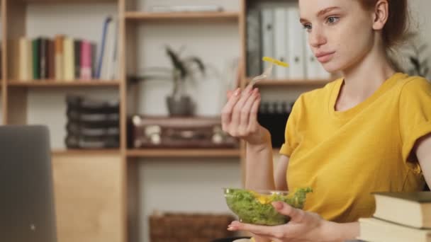 Calm Young Redhead Woman Eating Salad While Watching Her Laptop — Stock Video