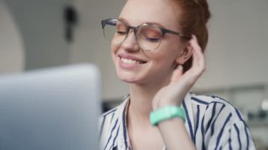 Pozitif kızıl saçlı bir kadın dairenin içinde dizüstü bilgisayarını kullanıyor.