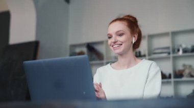 Mutlu bir kızıl saçlı kadın apartmanların içinde video bağlantısı ile konuşuyor.