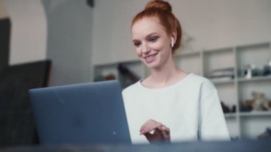 Güzel, kızıl saçlı bir kadın apartmanın içinde oturmuş video bağlantısıyla konuşuyor.