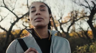 Genç ve mutlu bir Afrikalı Amerikalı kadın dışarıda parkta yürürken müziği dinliyor.