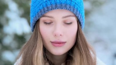 Mavi şapkalı mutlu genç bir kadının yakın çekim görüntüsü, kışın Central Park 'ın dışında yürürken kameraya poz veriyor.