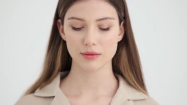 Güzel bir genç kadın kameraya bakıyor. Stüdyonun beyaz arka planında izole bir şekilde duruyor.