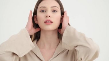 Çekici genç bir kadın kameraya poz veriyor. Stüdyoda beyaz arka planda tek başına duruyor.