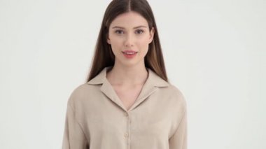 Pozitif bir genç kadın elini kameraya doğru sallıyor. Stüdyonun beyaz arka planında tek başına duruyor.