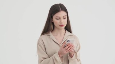 Stüdyoda beyaz arka planda duran akıllı telefonunu kullanan mutlu bir genç kadın.