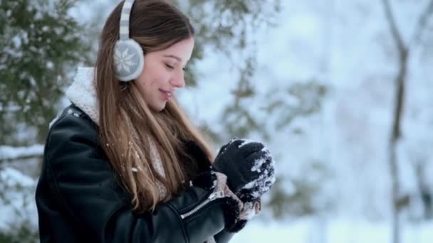 青い冬の帽子をかぶった笑顔の若い女性が冬に公園の外を歩く雪玉を作っています — ストック動画