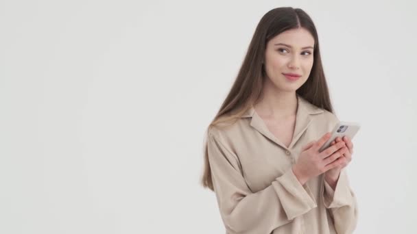 Uśmiechnięta Młoda Kobieta Używa Swojego Smartfona Stojącego Boku Odizolowanego Białym — Wideo stockowe