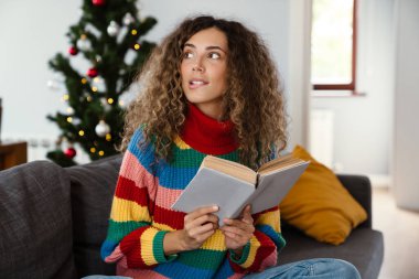 Rahat bir odada kanepede oturmuş kitap okuyan çok çekici bir kadın.