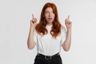 Ginger güzel, şok olmuş bir kız beyaz arka planda, parmaklarını yukarı kaldırarak bağırıyor.