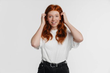 Kızıl güzel mutlu kız beyaz arka planda izole edilmiş kameraya poz veriyor ve gülümsüyor.