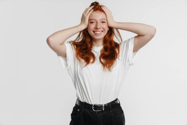 Ginger güzel mutlu kız başını tutuyor ve gülümsüyor beyaz arka planda.