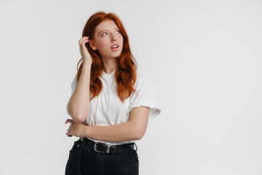 Kızıl saçlı güzel ciddi kız beyaz arka planda izole edilmiş ve yukarı bakıyor.