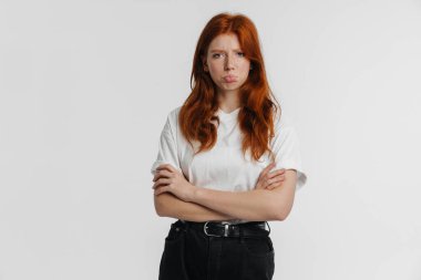 Ginger güzel mutsuz kız kollarını kavuşturup beyaz arka planda yalnız poz veriyor.