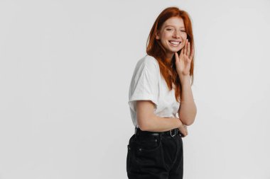 Kızıl güzel mutlu kız beyaz arka planda izole edilmiş kameraya poz veriyor ve gülümsüyor.