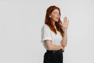 Kızıl, güzel, şaşkın, el sallayan, poz veren, beyaz arka planda yalnız bir kız.