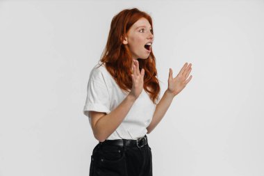 Kızıl saçlı, güzel, şok olmuş bir kız beyaz arka planda saklanarak şaşırdığını ifade ediyor.